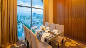 Un coin repas avec une table dressée pour six personnes, de grandes fenêtres et une vue sur le paysage urbain.
