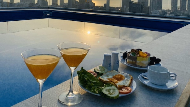 Une terrasse sur le toit offrant une vue panoramique sur la ville, deux verres à martini, une assiette de nourriture et des condiments.