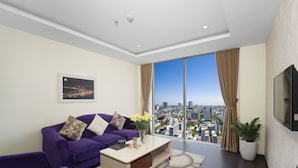 Un salon moderne avec un canapé violet, une table basse et une grande fenêtre donnant sur la ville.