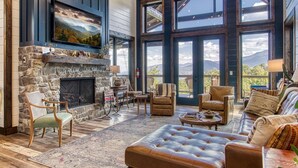 A spacious living room with a stone fireplace, large windows, and comfortable seating.