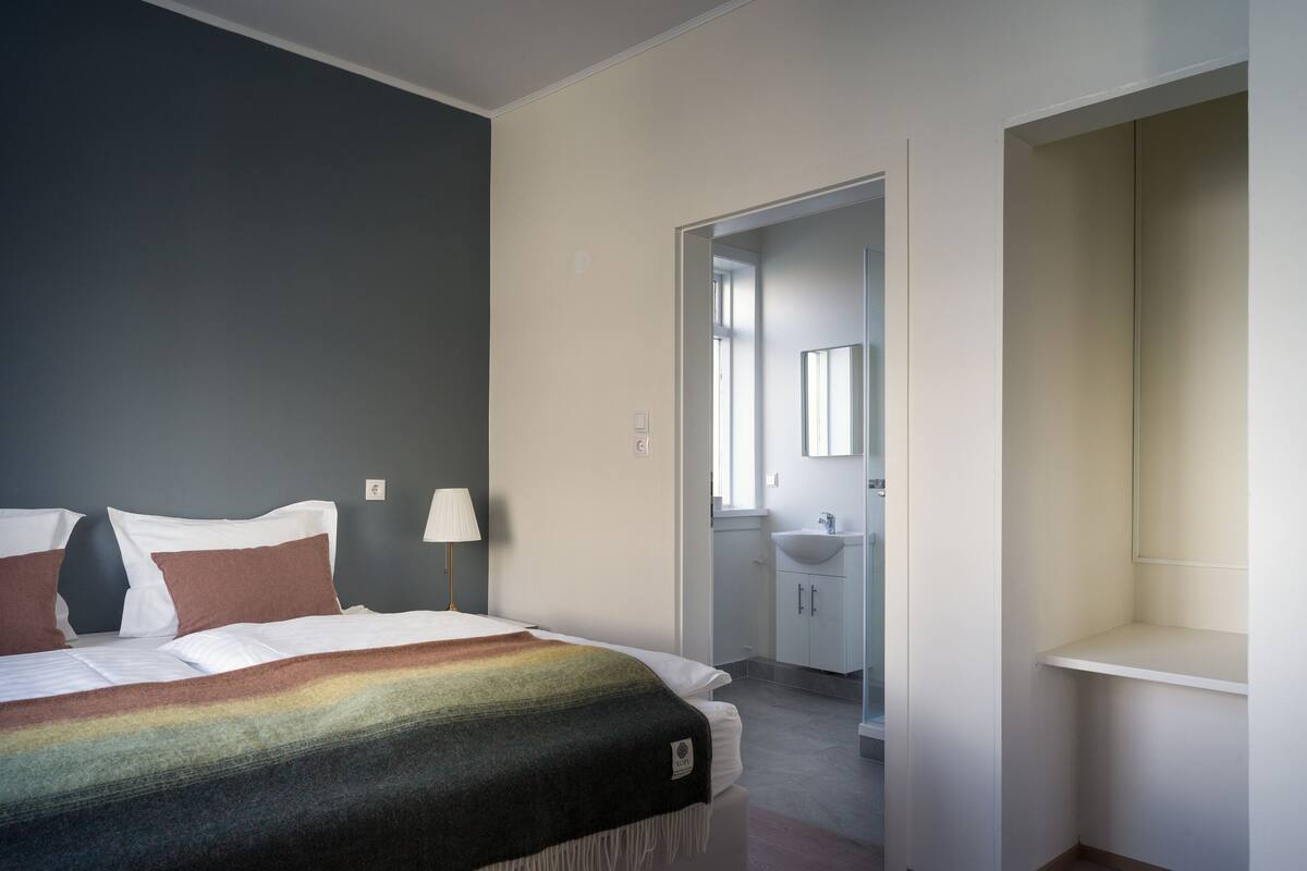 A bedroom with a bed, bedside lamps, and a bathroom visible through an open door.