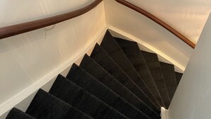 A staircase with dark carpeted steps and wooden handrails, leading to a landing with white walls and a small window. - Salt Guesthouse (Siglufjörður)