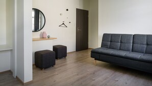 A modern living room with a grey sofa, two dark ottomans, a wooden floor, a mirror, a small pink vase, and a door. - Salt Guesthouse (Siglufjörður)