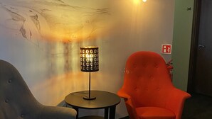 A room with a mural, a table with a lamp, and two chairs. - Salt Guesthouse (Siglufjörður)