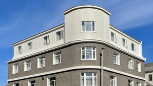 A multi-story building with a curved corner design, featuring a mix of window styles and a prominent cylindrical section on the top. - Salt Guesthouse (Siglufjörður)