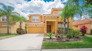 A two-story house with a garage, surrounded by a well-maintained lawn and various plants. - 4BR Disney Home w/ Private Pool • Sleeps 11 (Kissimmee)