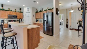 A modern kitchen with wooden cabinets, a stainless steel refrigerator, and a central island with bar stools. - 4BR Disney Home w/ Private Pool • Sleeps 11 (Kissimmee)