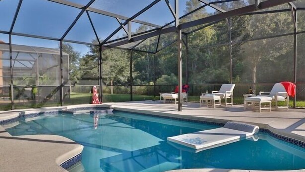 A covered swimming pool with lounge chairs and a patio area. - 4BR Disney Home w/ Private Pool • Sleeps 11 (Kissimmee)