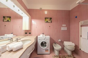 Une salle de bain avec des carreaux roses, un lave-linge, un bidet, des toilettes et un lavabo avec un miroir.