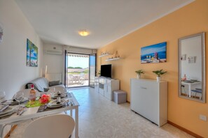 Un salon moderne comprenant un coin repas, un téléviseur et un balcon aménagé avec du mobilier d’extérieur.