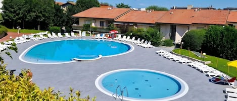 A pool area with two circular pools, lounge chairs, and a building with a tiled roof.
