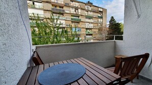 Ein Balkon mit Holztisch und -stühlen, einer blauen Matte und Blick auf ein mehrstöckiges Gebäude.