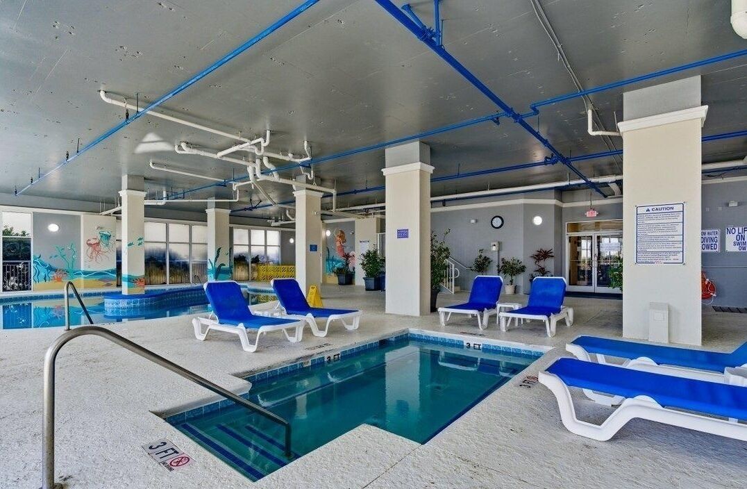 Une piscine intérieure avec des chaises longues bleues, un plongeoir et des panneaux de sécurité.