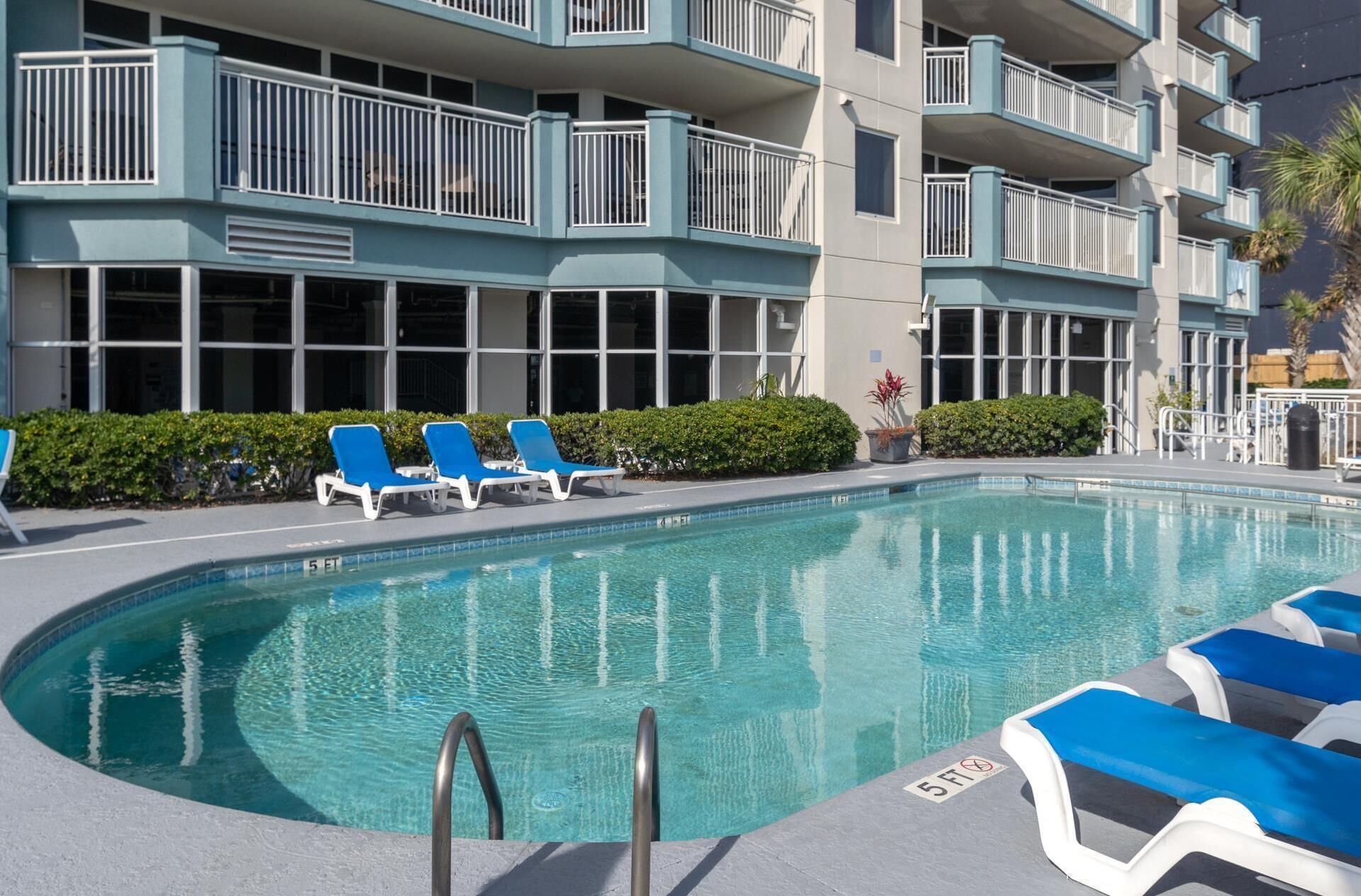 A pool area with blue lounge chairs, a clear pool, and a building with balconies.