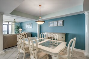 Een eethoek met een tafel met glazen blad, witte stoelen en een witte kast.