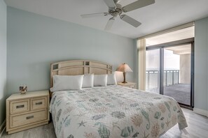 Een slaapkamer met een bed, nachtkastjes, een plafondventilator en uitzicht op een balkon.