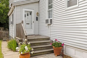Uma casa com varanda frontal, escada de madeira e dois vasos de plantas.