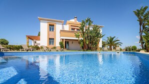 A large swimming pool with clear blue water, surrounded by lounge chairs and palm trees. - Quinta Dionysus | 6 Bedrooms | Own Vineyard | Albufeira (Albufeira)