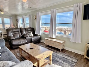 Un salon avec un canapé en cuir, une table basse en bois et une vue sur la plage grâce à de grandes fenêtres.
