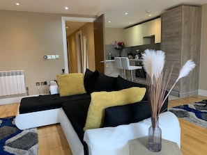 A modern living room with a sectional sofa, a dining area, and a kitchen in the background.
