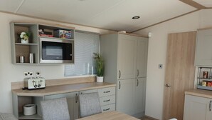 A compact kitchen with a wooden table and chairs, a built-in oven, and cabinets. - The Sea Breeze - Captivating Caravan in Camber (Rye)