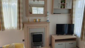 A living room with a fireplace, television, and wooden cabinets. - The Sea Breeze - Captivating Caravan in Camber (Rye)