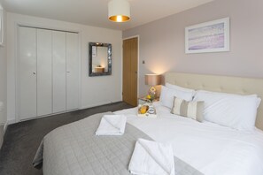 A hotel room with a large bed, a bedside table with a lamp, a mirror, and a framed picture on the wall. - Stunning 2 bed Seaside Apartment With Sea Views (Bournemouth)