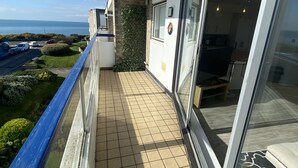 Een balkon met betegelde vloer, een glazen deur naar een kamer en uitzicht op zee.