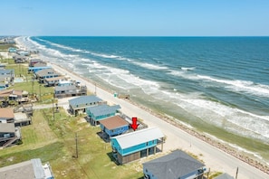 A coastal residential area with houses along the beach, a clear sky, and a calm sea.