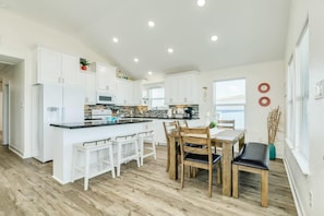 A modern kitchen with white cabinets, a central island, and a dining area with wooden chairs and a table.
