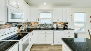 A kitchen with white cabinets, a black countertop, a stove, and a microwave. - Sea Forever - Front Row, Fire Pit & Miles of Surf! (Surfside Beach)