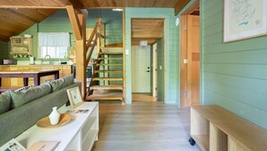 Un interior acogedor con una escalera de madera, una pared verde y un área de comedor con una mesa y sillas de madera.