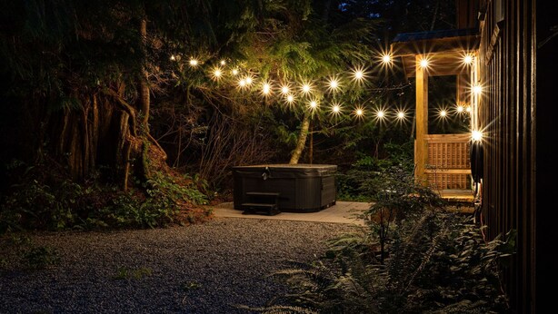 Un espacio al aire libre techado con un jacuzzi, rodeado de árboles y luces colgantes.