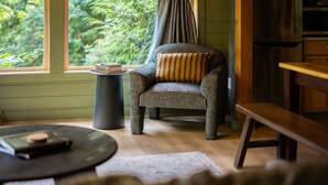Una habitación acogedora con un sillón estampado, una mesita con libros y vistas a zonas verdes por la ventana.
