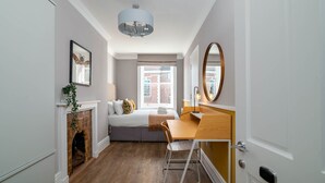 A bedroom with a bed, a desk, a chair, a fireplace, a window, and a door. - 37 Doughty Street (London)
