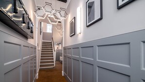 A hallway with a carpeted floor, white paneled walls, a staircase, and modern geometric light fixtures. - 37 Doughty Street (London)