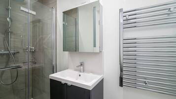 A modern bathroom with a glass-enclosed shower, a white sink, and a chrome towel rack.