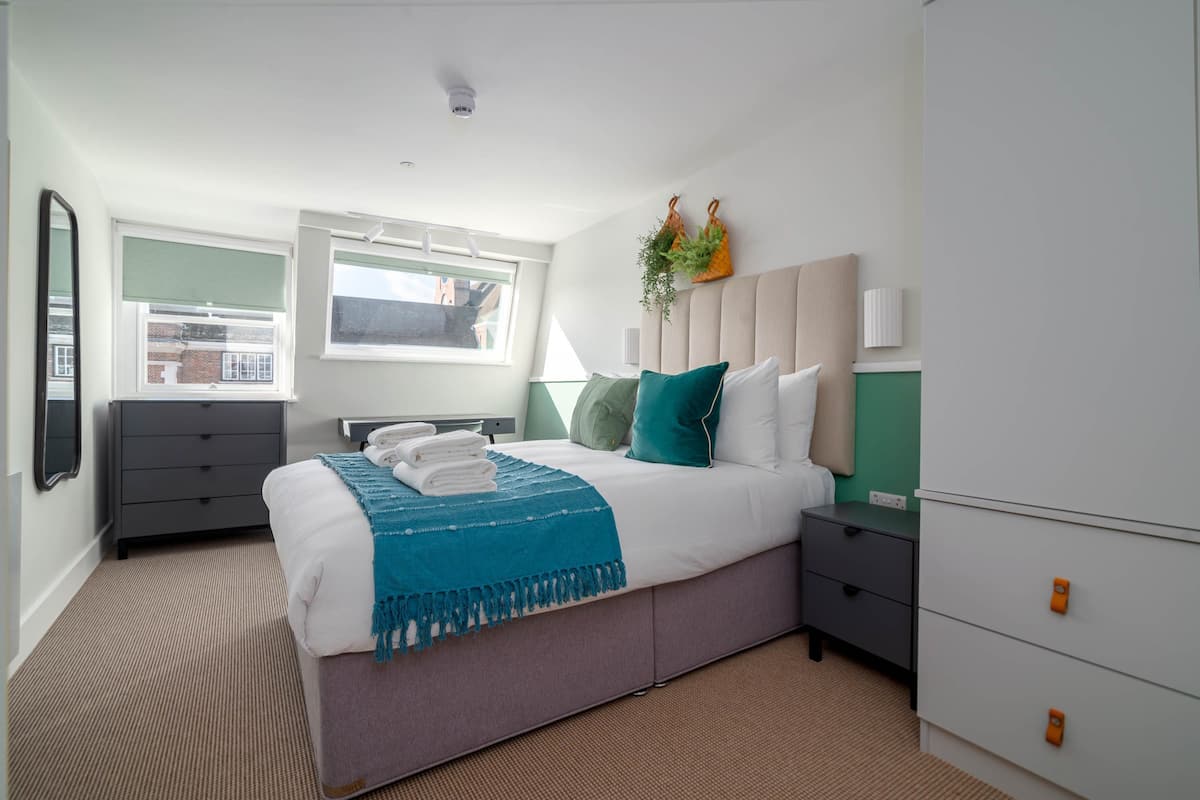 A modern bedroom with a bed, bedside tables, a dresser, a window, and a plant.
