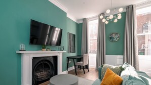 A living room with teal walls, a fireplace, a television, and a large window with curtains. - 37 Doughty Street (London)