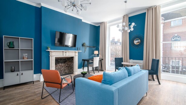 A modern living room with a blue wall, a fireplace, a sofa, and a television. - 37 Doughty Street (London)