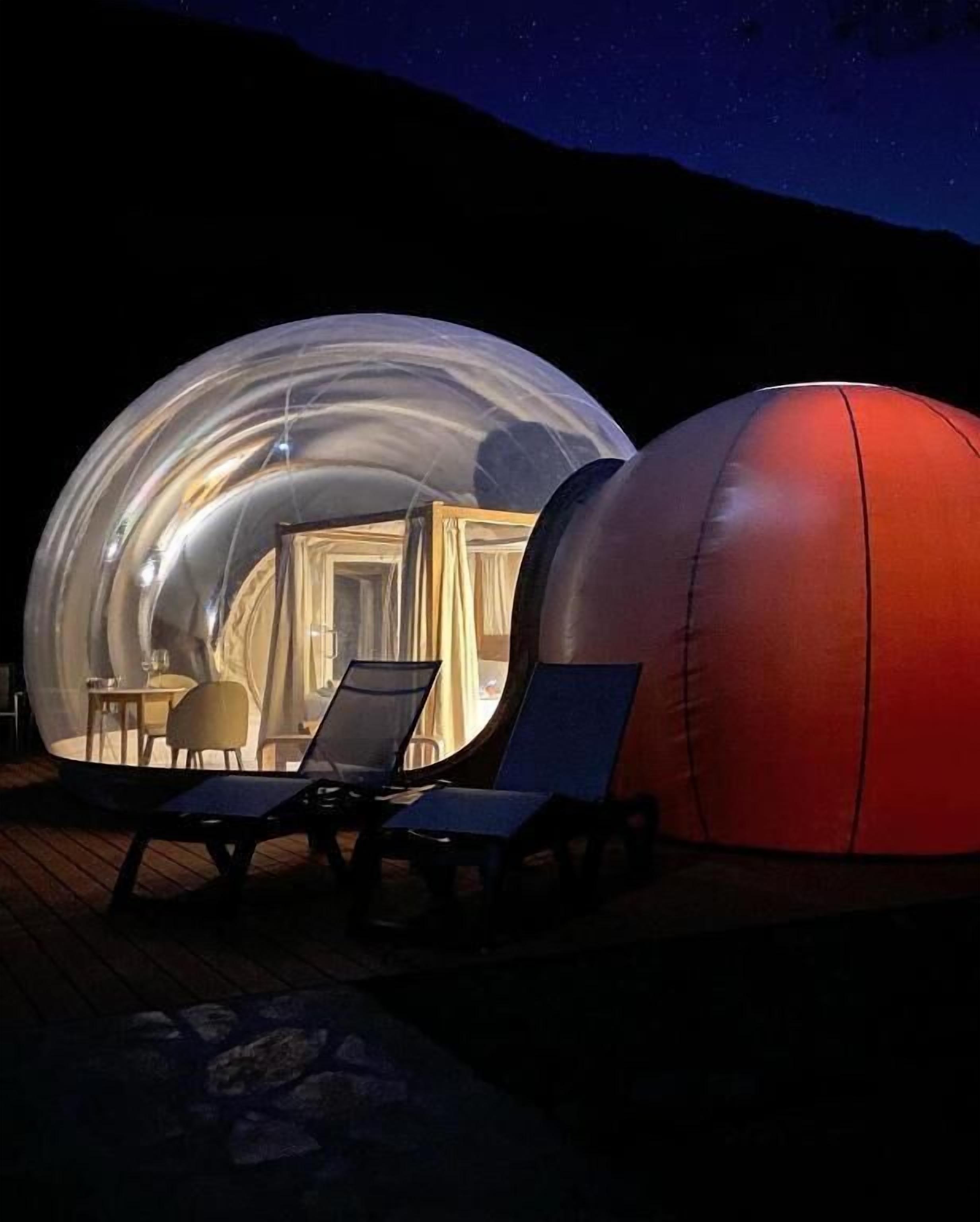 Dos estructuras esféricas, una transparente y otra opaca, con zonas de estar y una mesa visibles en su interior.