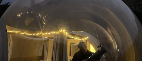 Ein Zimmer mit einer transparenten Kuppel, einem Bett, Vorhängen und Lichterketten.