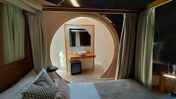 Una habitación circular con una cama, una mesita, un lavamanos y un espejo.