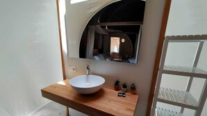 Un baño con lavamanos blanco, encimera de madera y un espejo encima. Hay pequeñas plantas en macetas sobre la encimera.