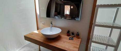 A bathroom with a white sink, wooden countertop, and a mirror above it. There are small potted plants on the countertop.