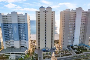 A high-rise hotel with multiple floors, a beach view, and a parking area with a few cars.