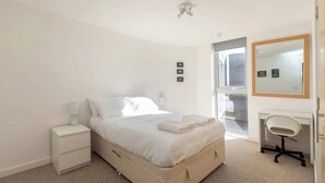 Un dormitorio con cama, mesita de noche y escritorio con silla.