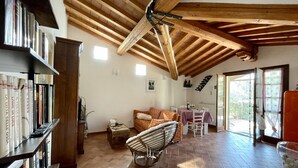 A spacious room with a high wooden ceiling, a cozy seating area with a sofa and a chair, a bookshelf, and a dining table with chairs. - Casa Sophia, pool with sea view - garden, barbecue and parking are pri (Guardistallo)