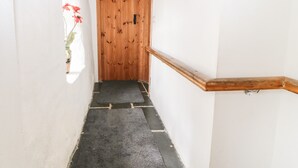 Un pasillo estrecho con una puerta de madera al final, una planta pequeña a la izquierda y un pasamanos de madera a la derecha.