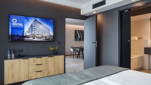 A modern hotel room with a large bed, a TV mounted on the wall, a wooden dresser, and a door leading to a bathroom. - Q Hotel Plus Wrocław Bielany (Kobierzyce)